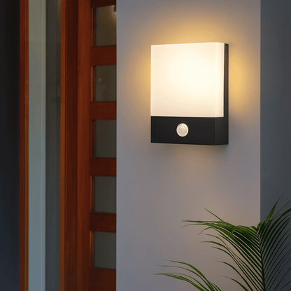 Modern outdoor wall light fixture on a white wall with a plant in the corner.
