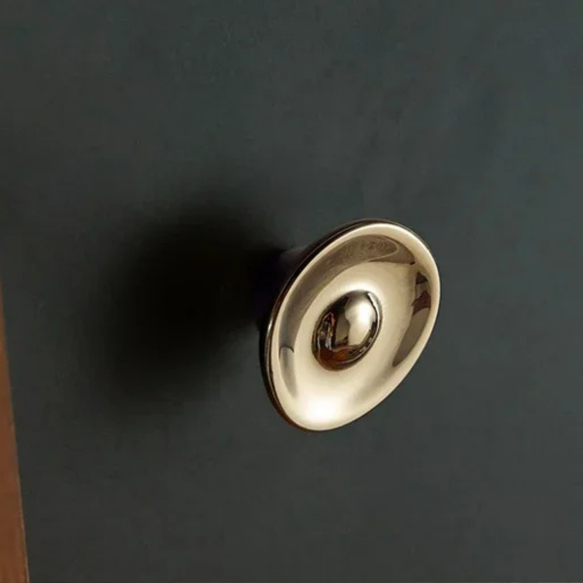 Polished metal dome-shaped knob installed on a dark-colored cabinet surface