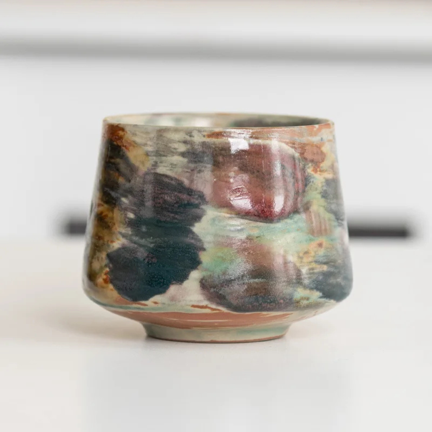Handcrafted ceramic cup featuring deep teal, brown, and earthy multicolored glaze patterns.