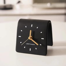 A black leather desk clock with gold hands and minimalist design sitting on a white surface.