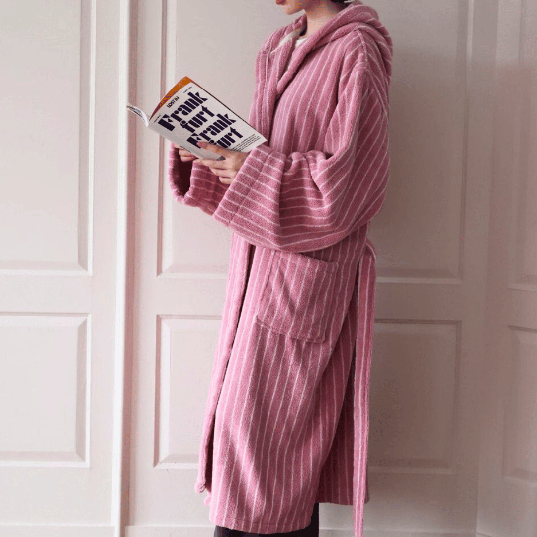 Person wearing a pink robe holding a book in front of a white door.