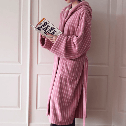 Person wearing a pink robe holding a book in front of a white door.