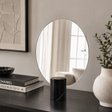 Round mirror on a wall with decor items including books and a vase.