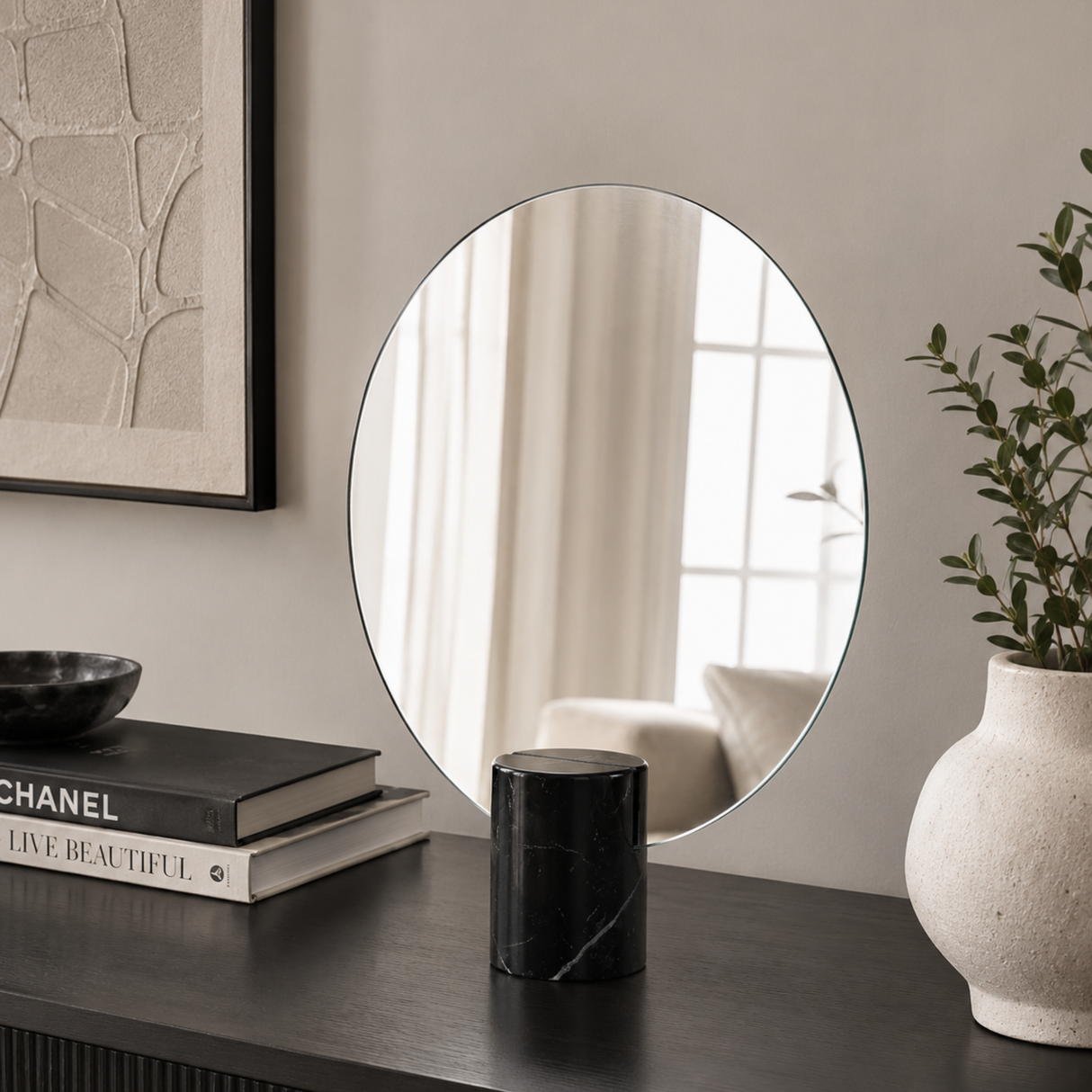 Round mirror on a wall with decor items including books and a vase.