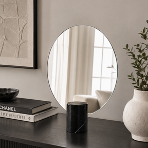Round mirror on a wall with decor items including books and a vase.