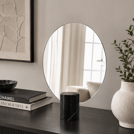 Round mirror on a wall with decor items including books and a vase.