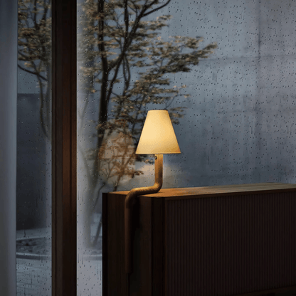 Modern lamp on a wooden surface with a textured wall and plant in the background