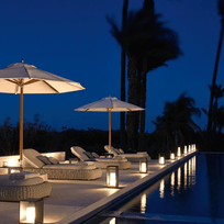Poolside area with lounge chairs, umbrellas, and candles at night.