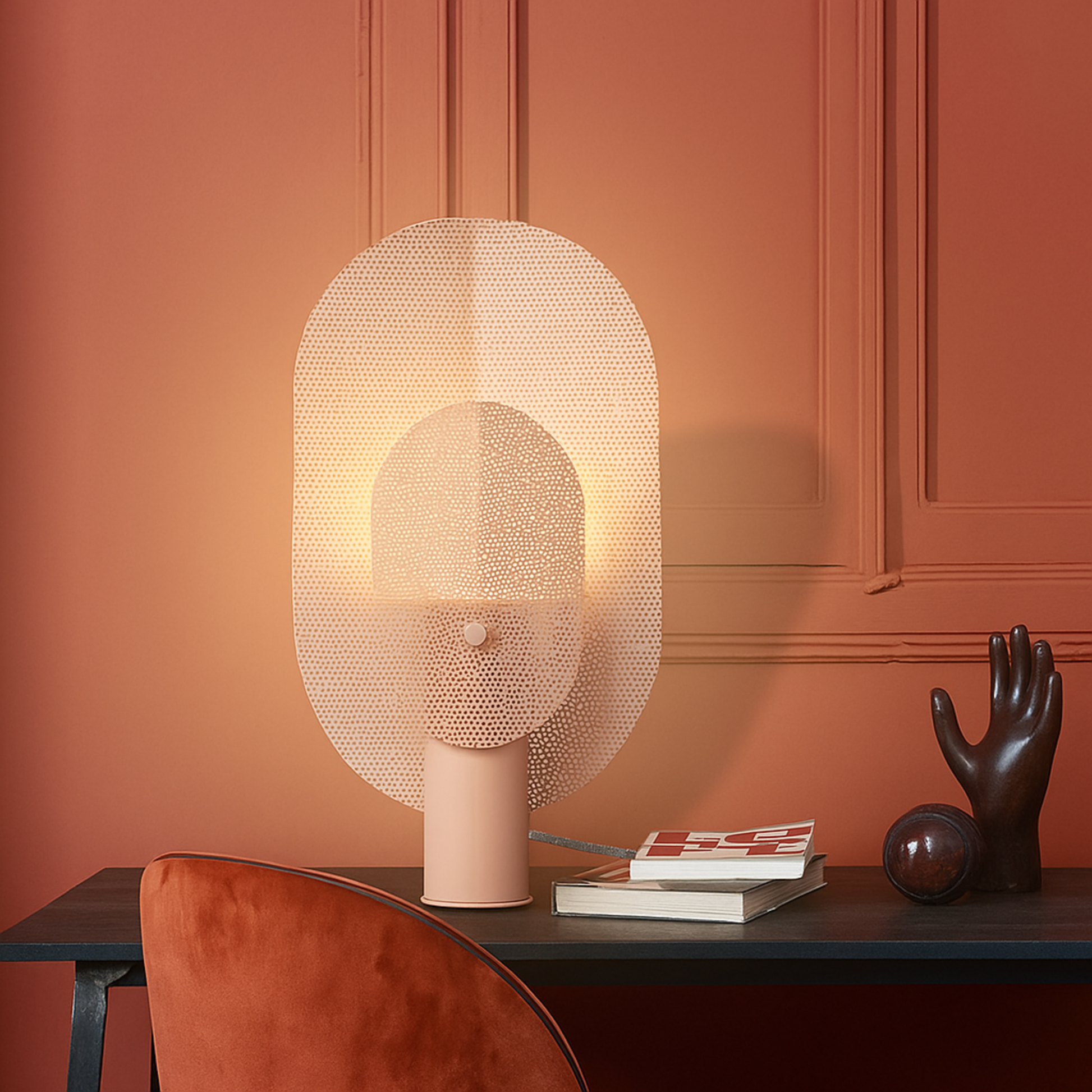 Decorative table lamp on a wooden surface with a warm glow against an orange wall.