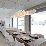 Modern dining area with a long wooden table set for dinner, white chairs, and a stylish pendant light.