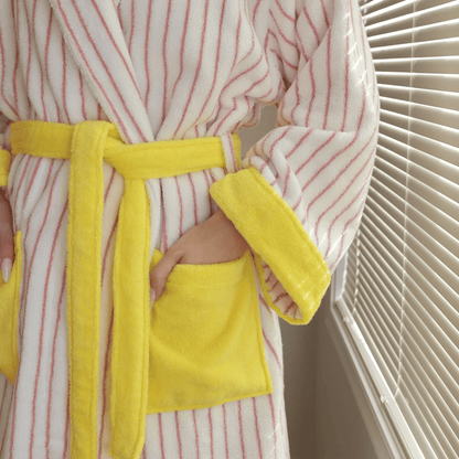 Person wearing a striped robe with yellow trim and pocket, standing in front of a window.