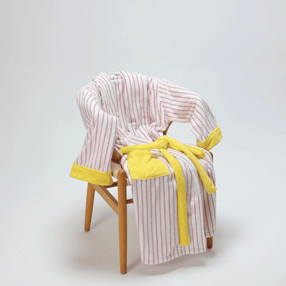 Striped robe with yellow trim draped over a wooden chair on a light gray background