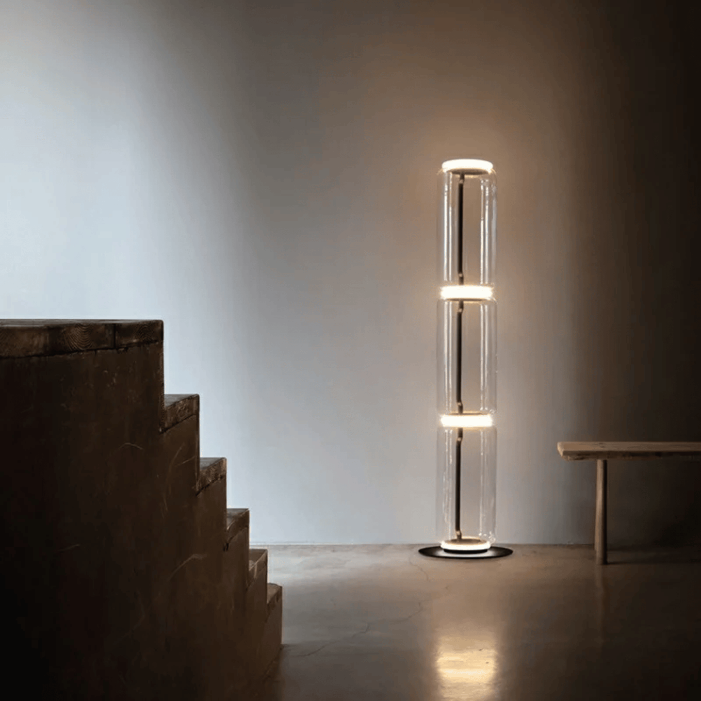Modern floor lamp with cylindrical design in a minimalistic room with stairs and table.