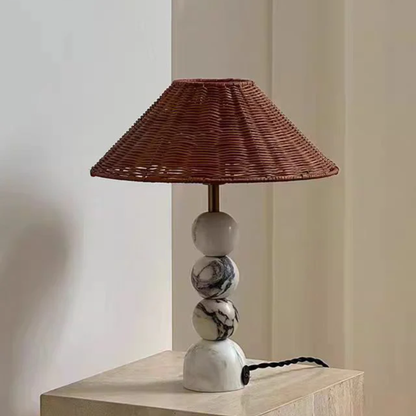 Table lamp with wicker shade and marble base on a wooden surface