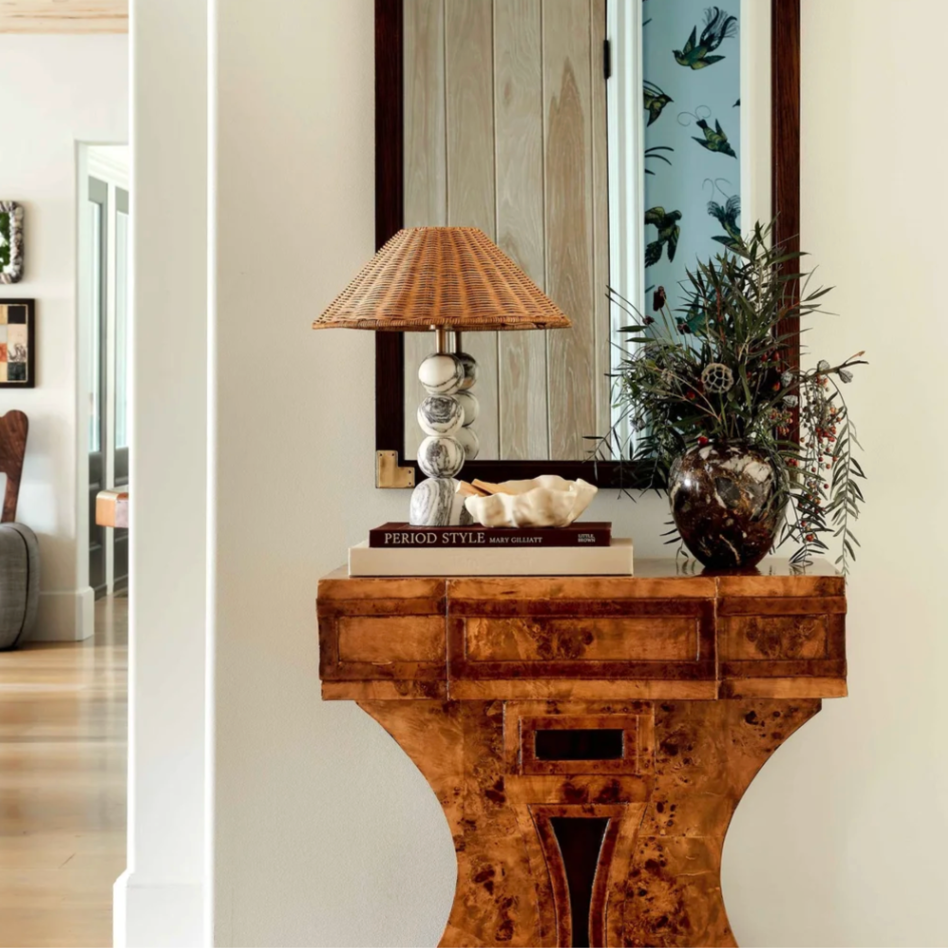 Wooden console table with decorative items including a lamp and books, against a neutral wall.