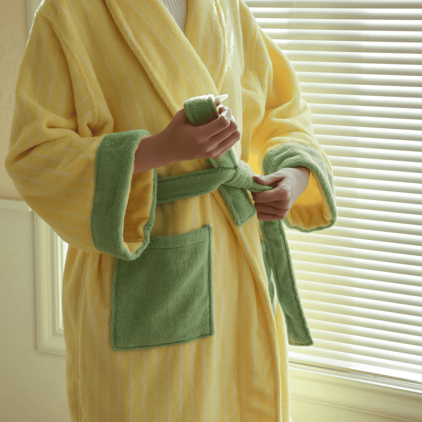 Person wearing a yellow and green robe holding a bottle of lotion.
