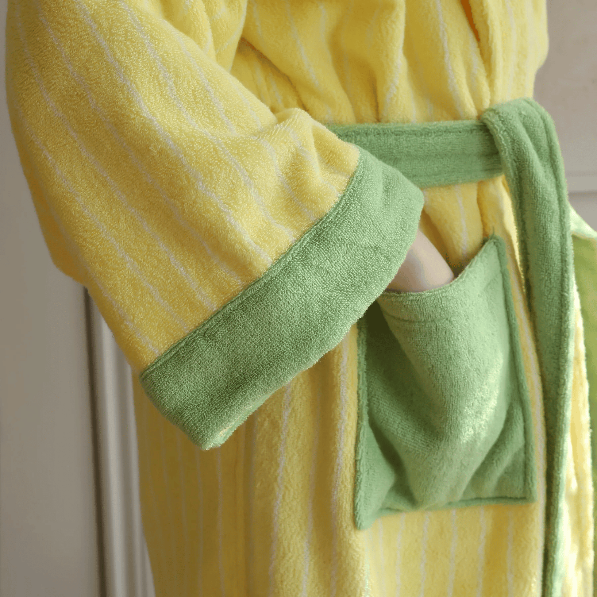 Yellow robe with green trim held by a person against a neutral background