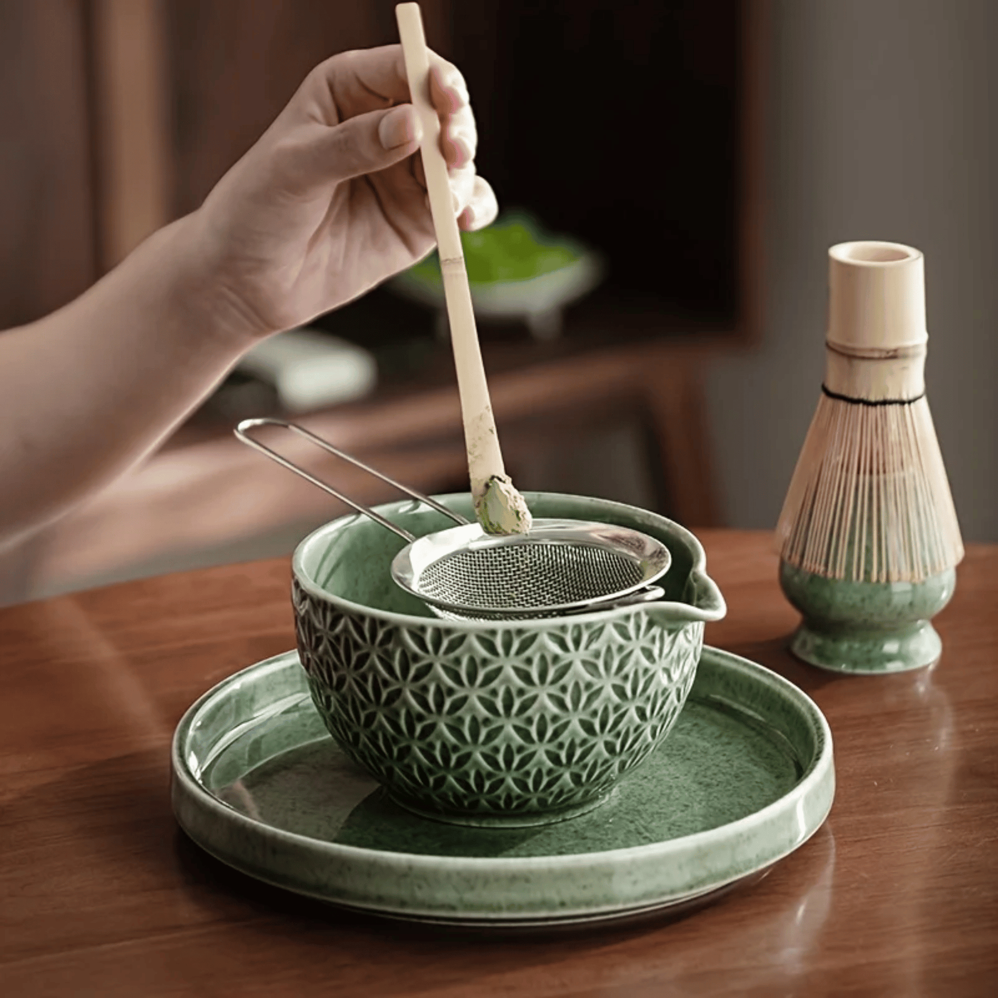 Green ceramic tea bowl with a strainer and wooden spoon on a wooden table.