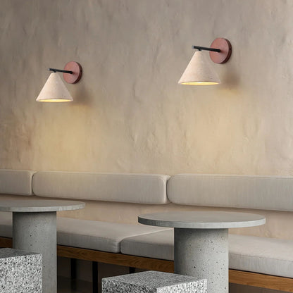 A pair of wooden wall sconces with white cone lampshades mounted in a dining or study area with light gray seating.