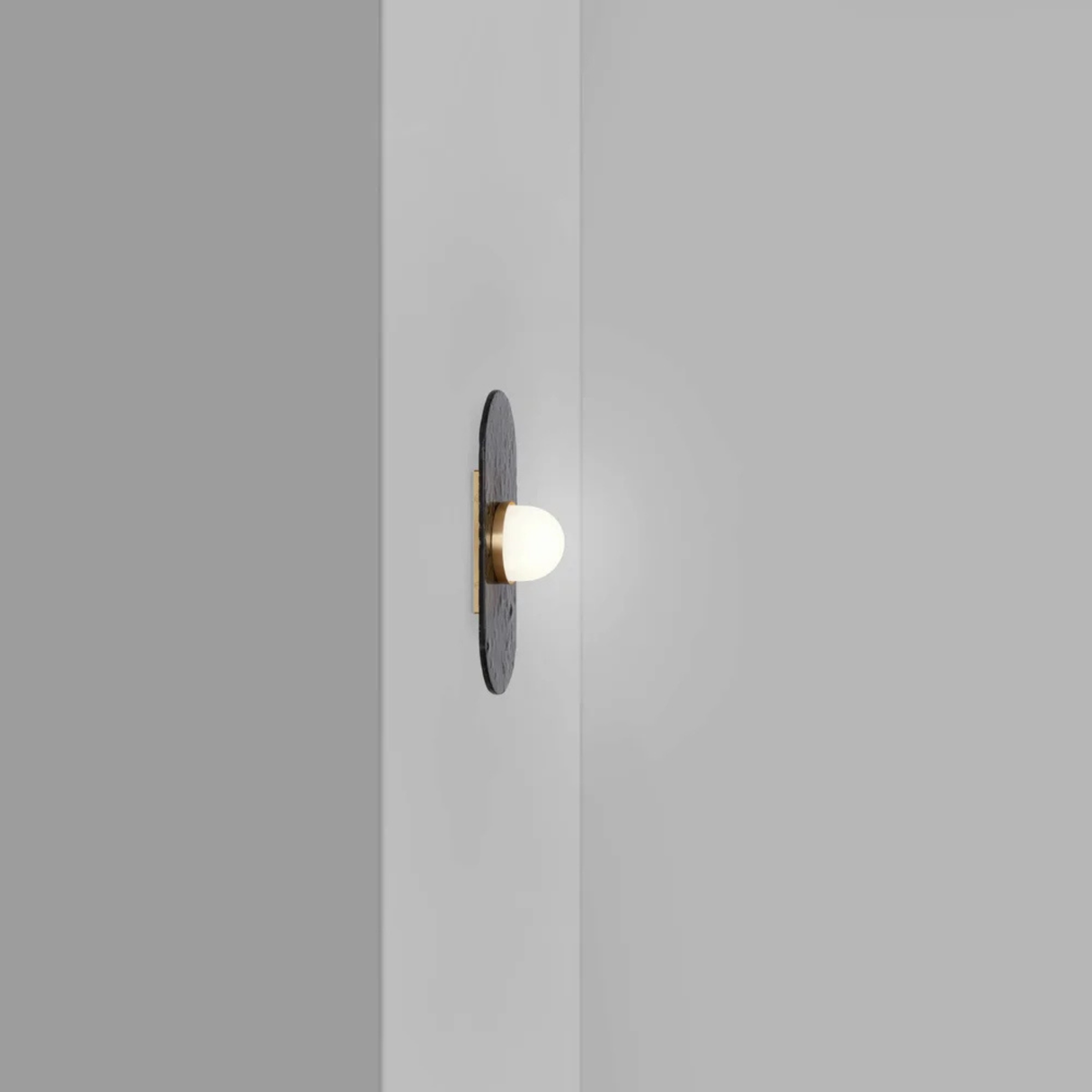 single bulb sconce with brass mount on dark raindrop textured backplate