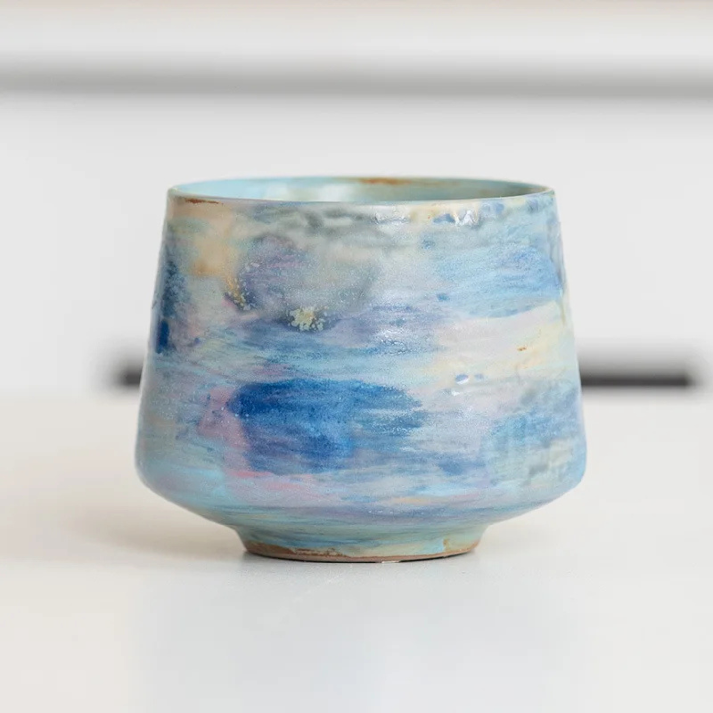 Ceramic cup with light pastel glazing in hues of blue, beige, and reddish brown.