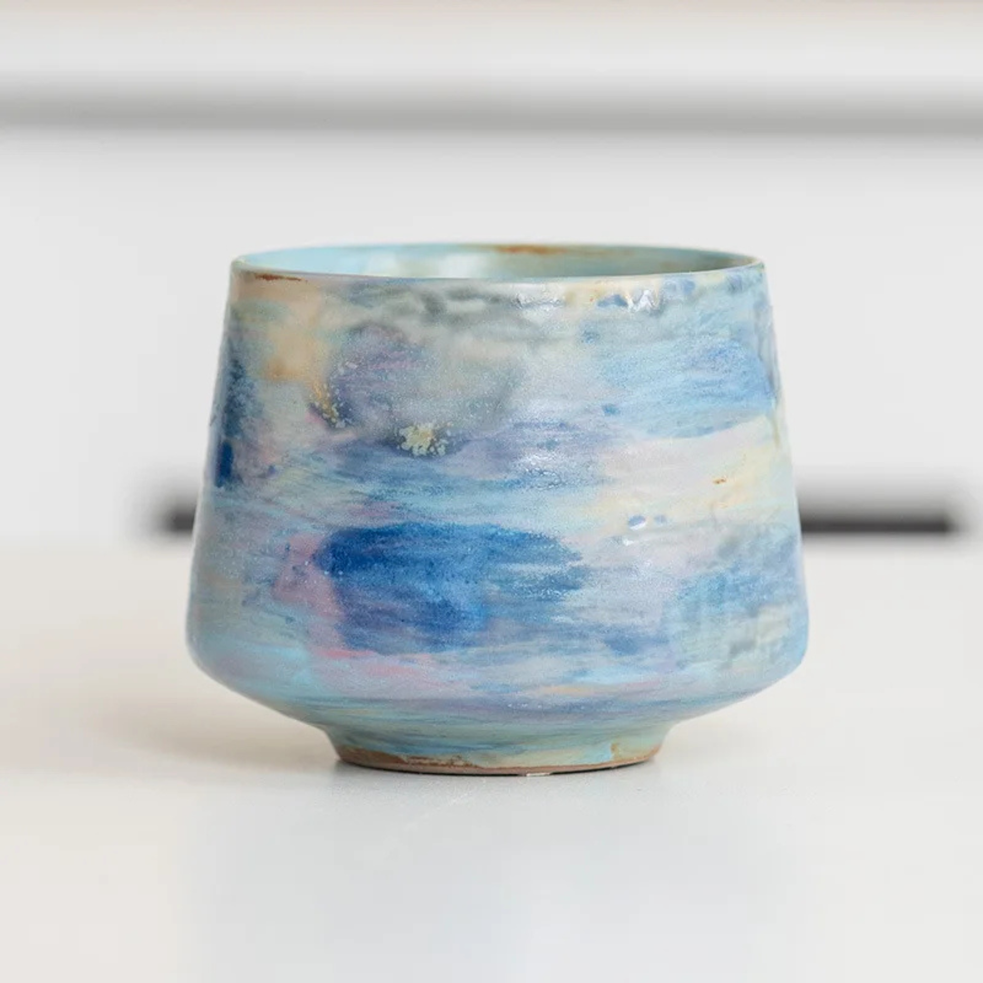 Ceramic cup with light pastel glazing in hues of blue, beige, and reddish brown.