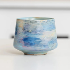 Ceramic cup with light pastel glazing in hues of blue, beige, and reddish brown.