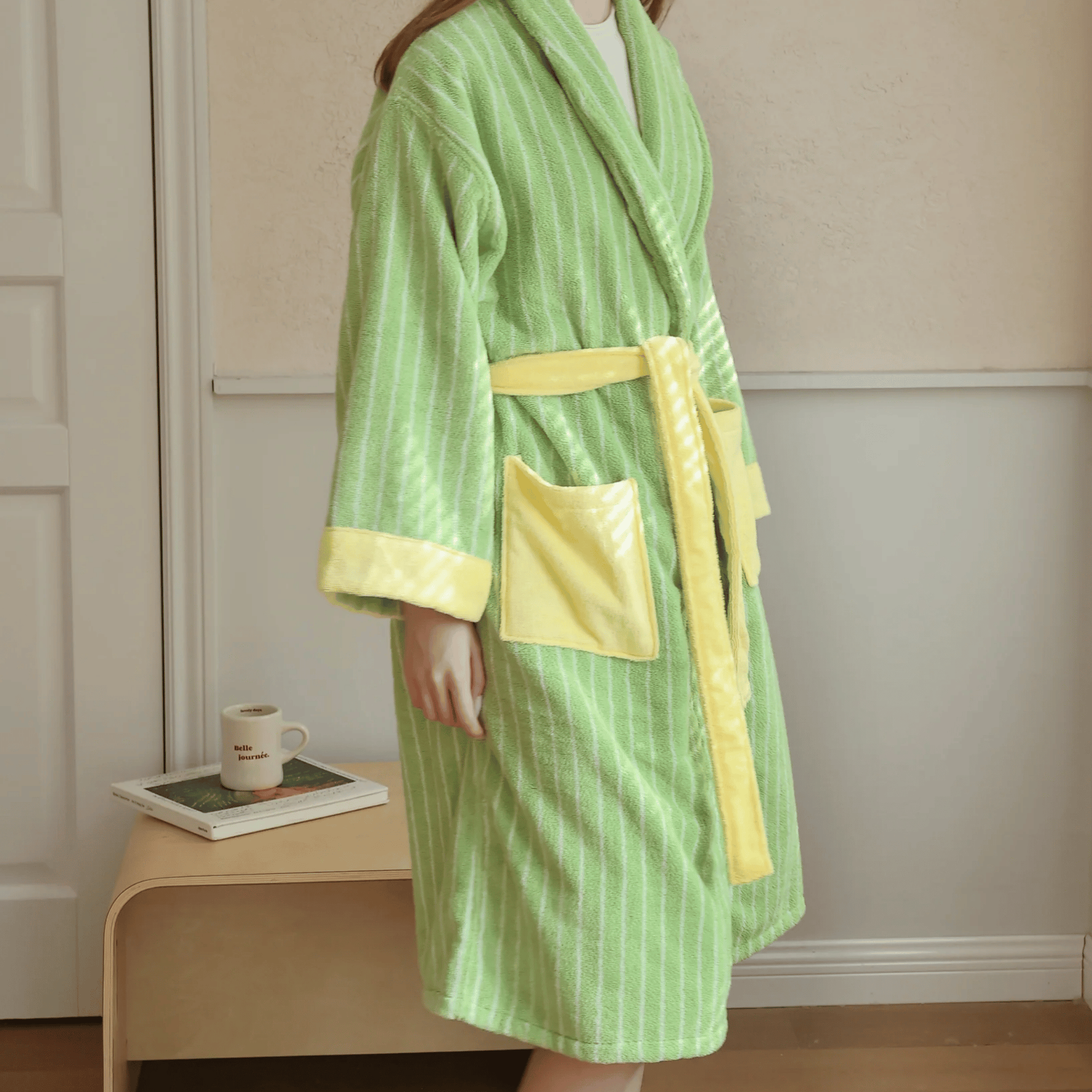Person wearing a green and yellow striped robe with a belt in a room.