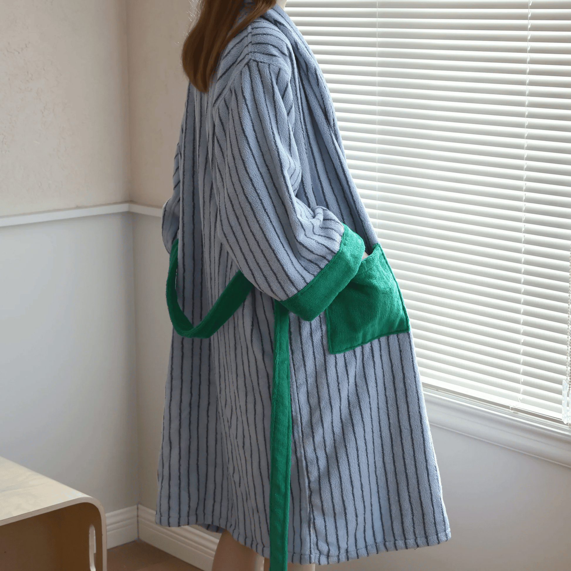 Person wearing a striped robe with green trim in a room with white walls and a window.