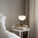 Modern table lamp on a marble side table next to a bed with neutral tones.