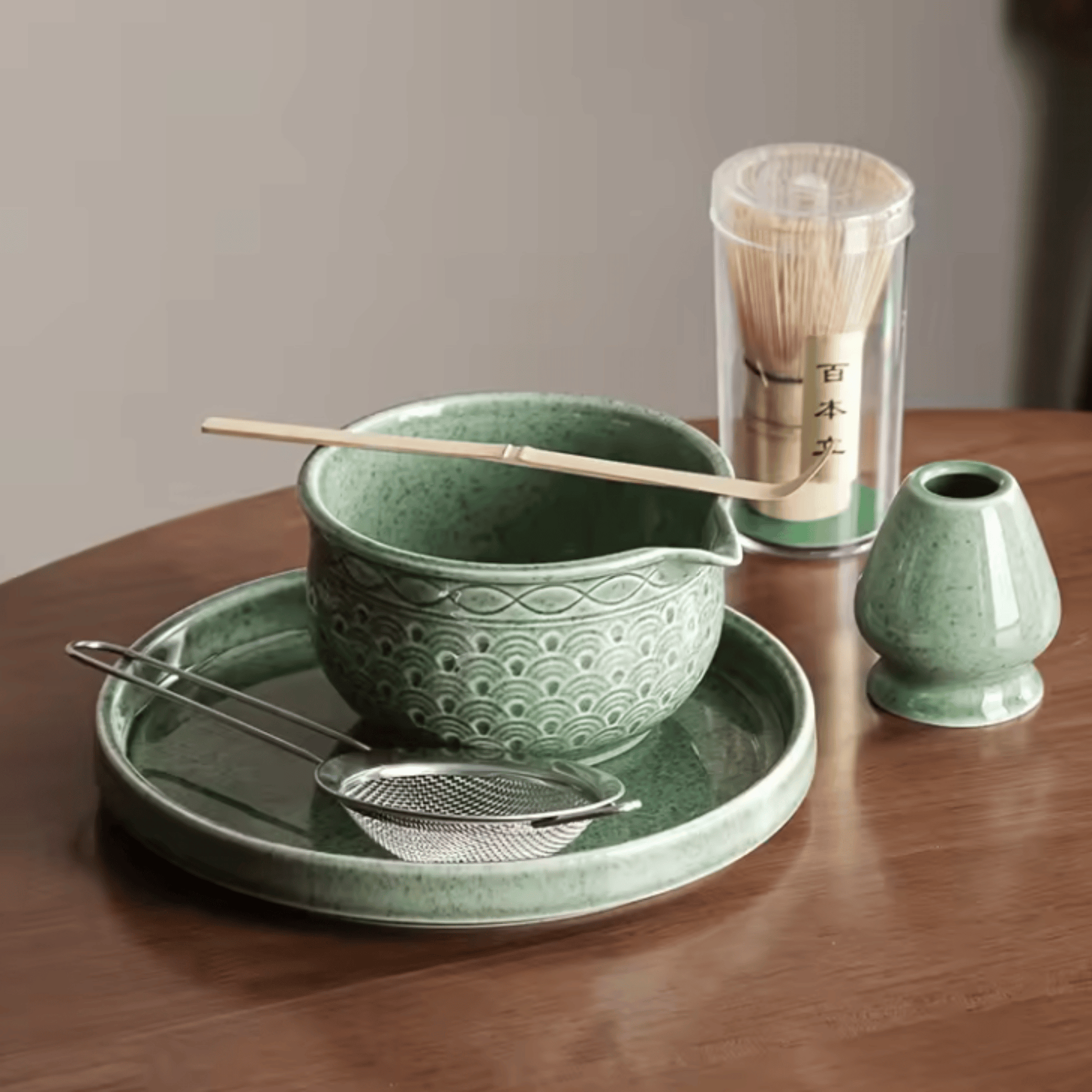 Green ceramic tea set with bowl, tray, whisk, and holder on a wooden table.