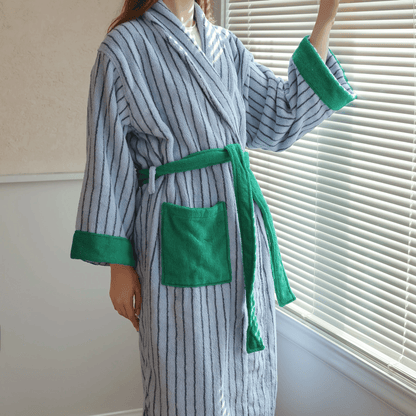 Person wearing a gray and green striped robe with a belt in a room with blinds.