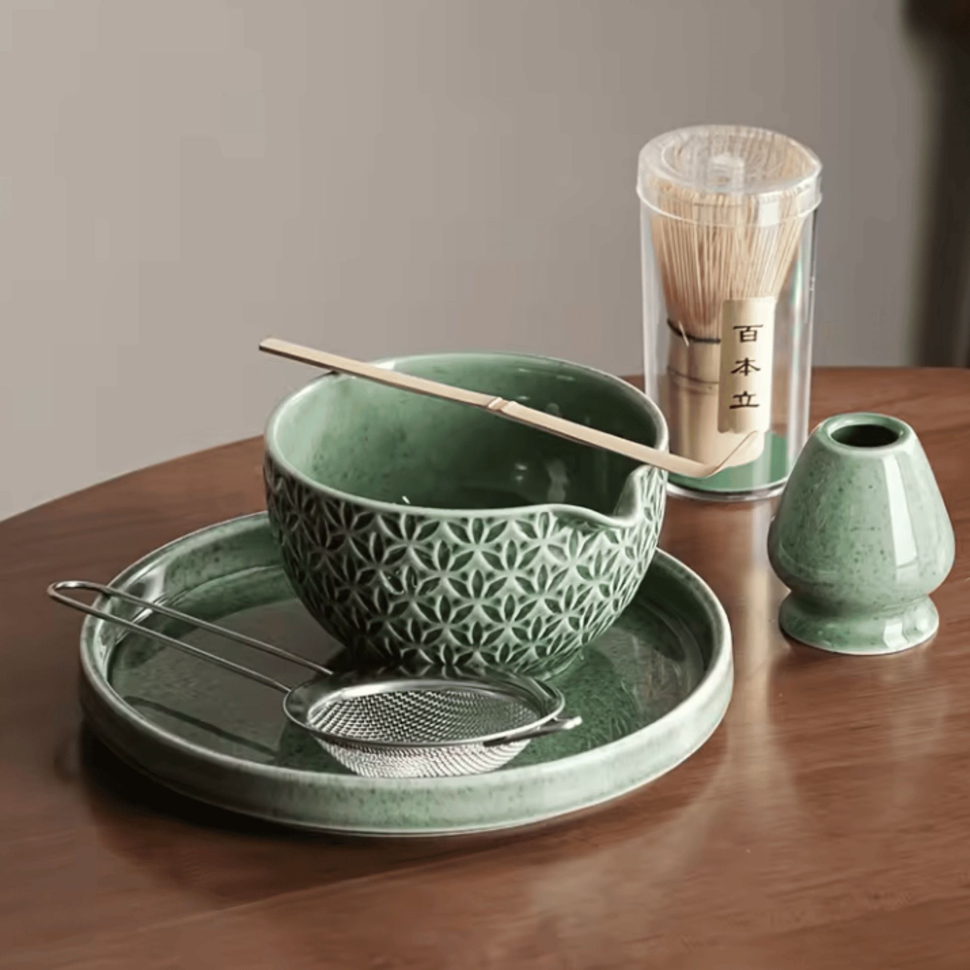 Green ceramic tea set with bowl, spoon, and container on a wooden table.