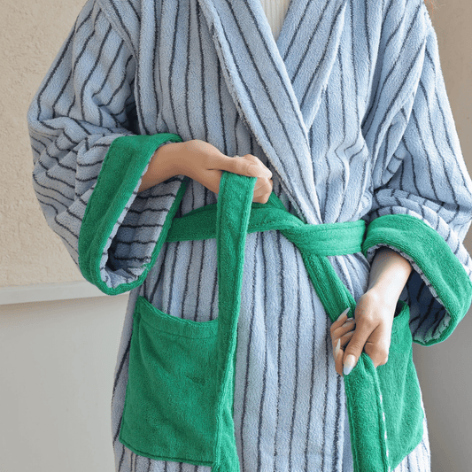 Person wearing a gray and white striped robe with green trim, holding a green towel.