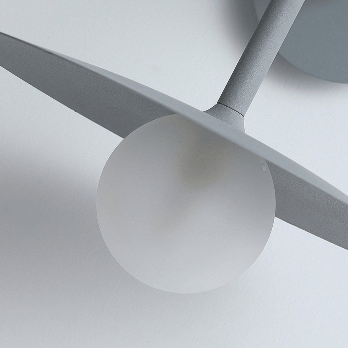 Close-up of a modern ceiling light fixture with gray blades and white sphere on a neutral background