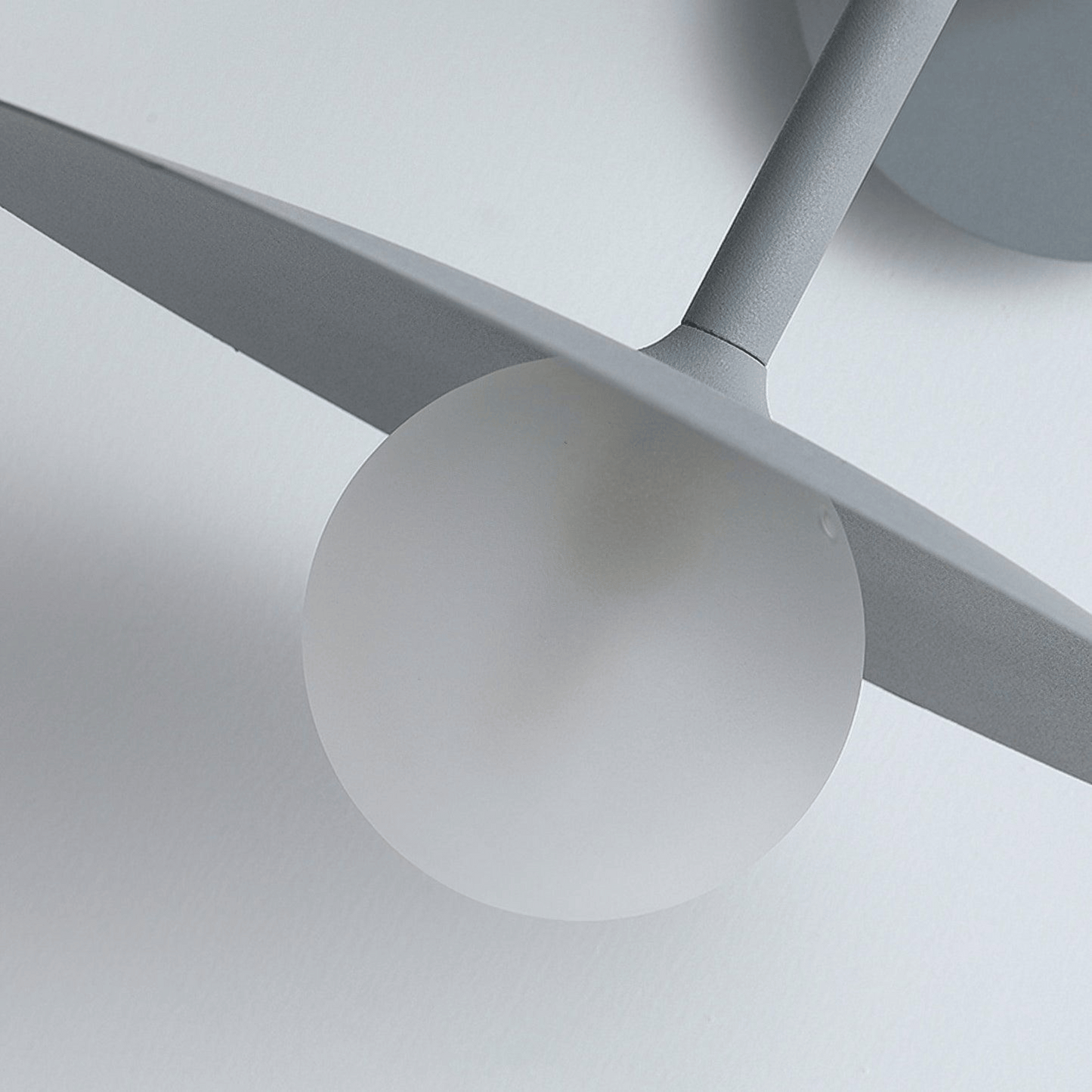 Close-up of a modern ceiling light fixture with gray blades and white sphere on a neutral background