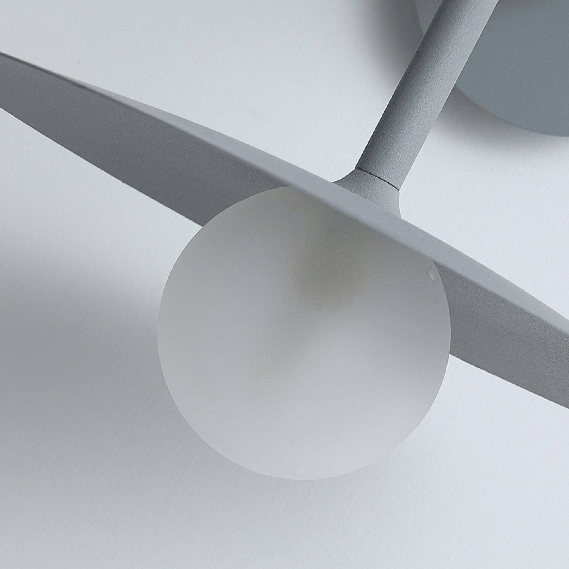 Close-up of a modern ceiling light fixture with gray blades and white sphere on a neutral background