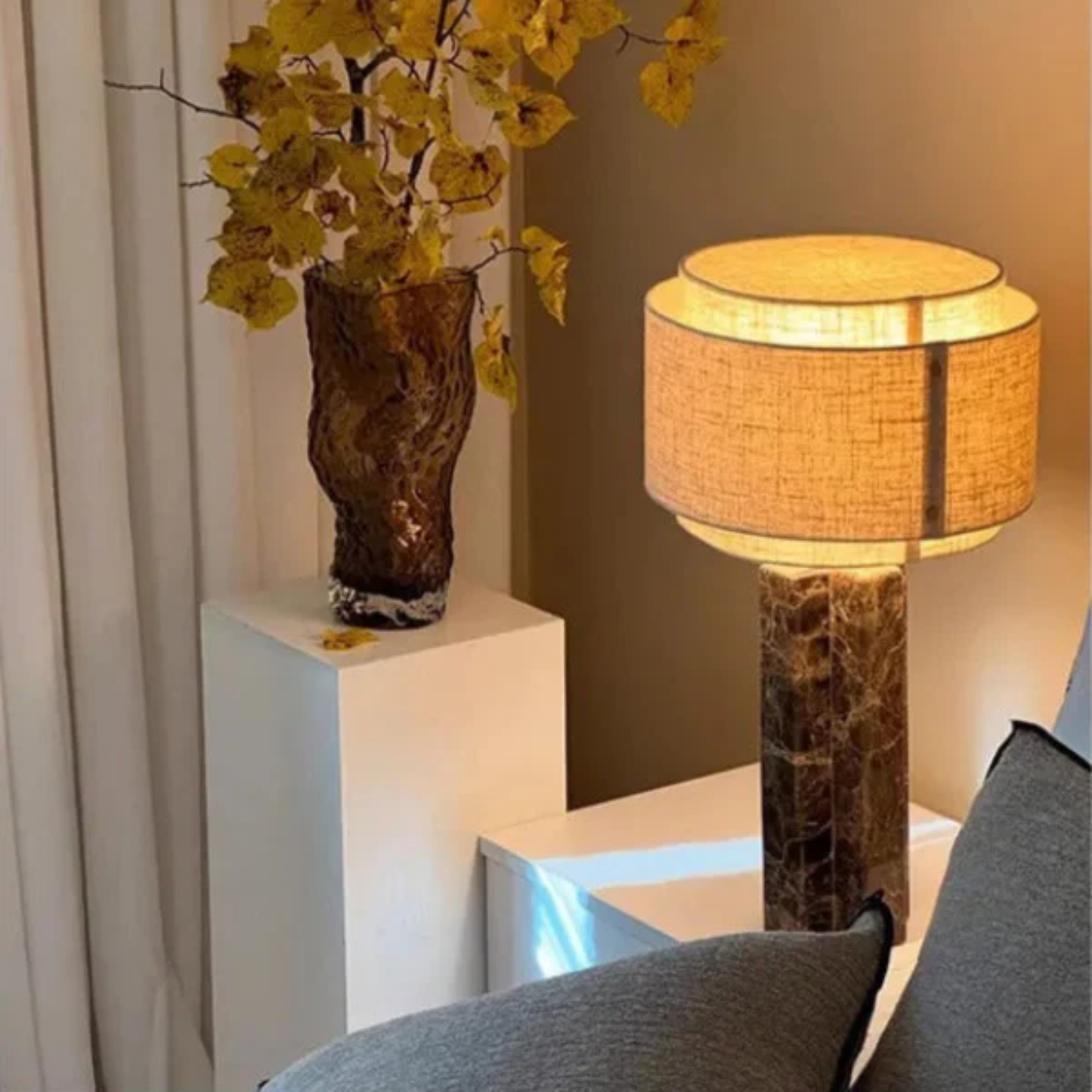 Decorative lamp with a textured base and yellow flowers in a vase on a white pedestal.