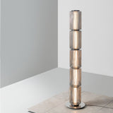 Ribbed-glass floor lamp placed beside long gray curtains near a seating area.