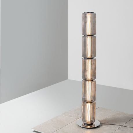 Ribbed-glass floor lamp placed beside long gray curtains near a seating area.
