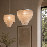 Two chandelier lights hanging on a wall with a painting and plant in the background.