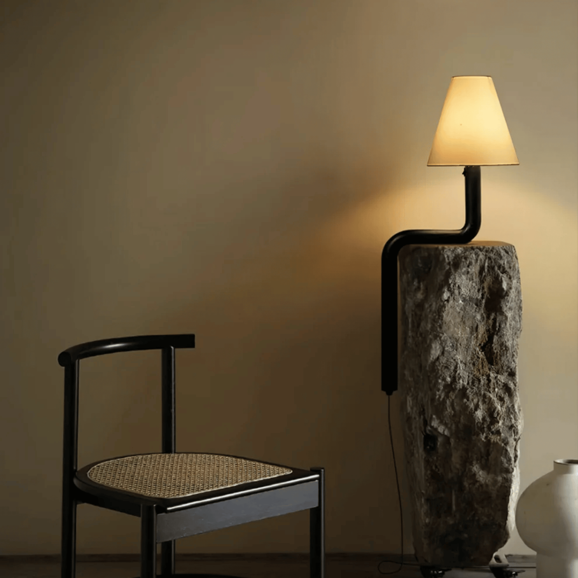 Modern wall lamp with black pipe design next to a black chair against a beige wall.