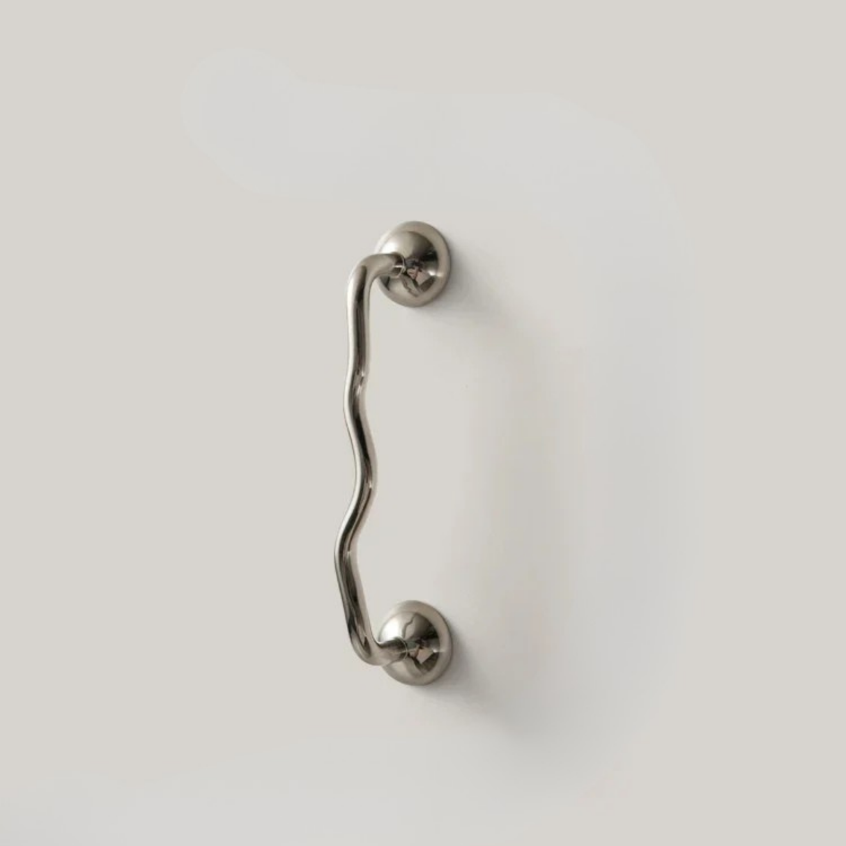 Shorter wavy stainless steel handle mounted on a minimal white surface