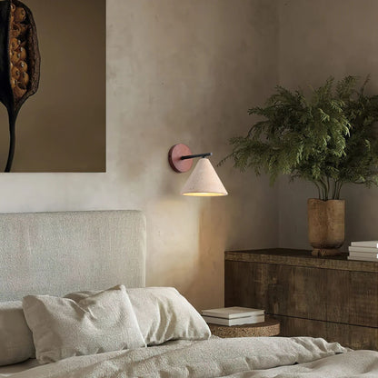 A wood-accented wall sconce with a white shade casting warm light above a bed in a serene, neutral bedroom.