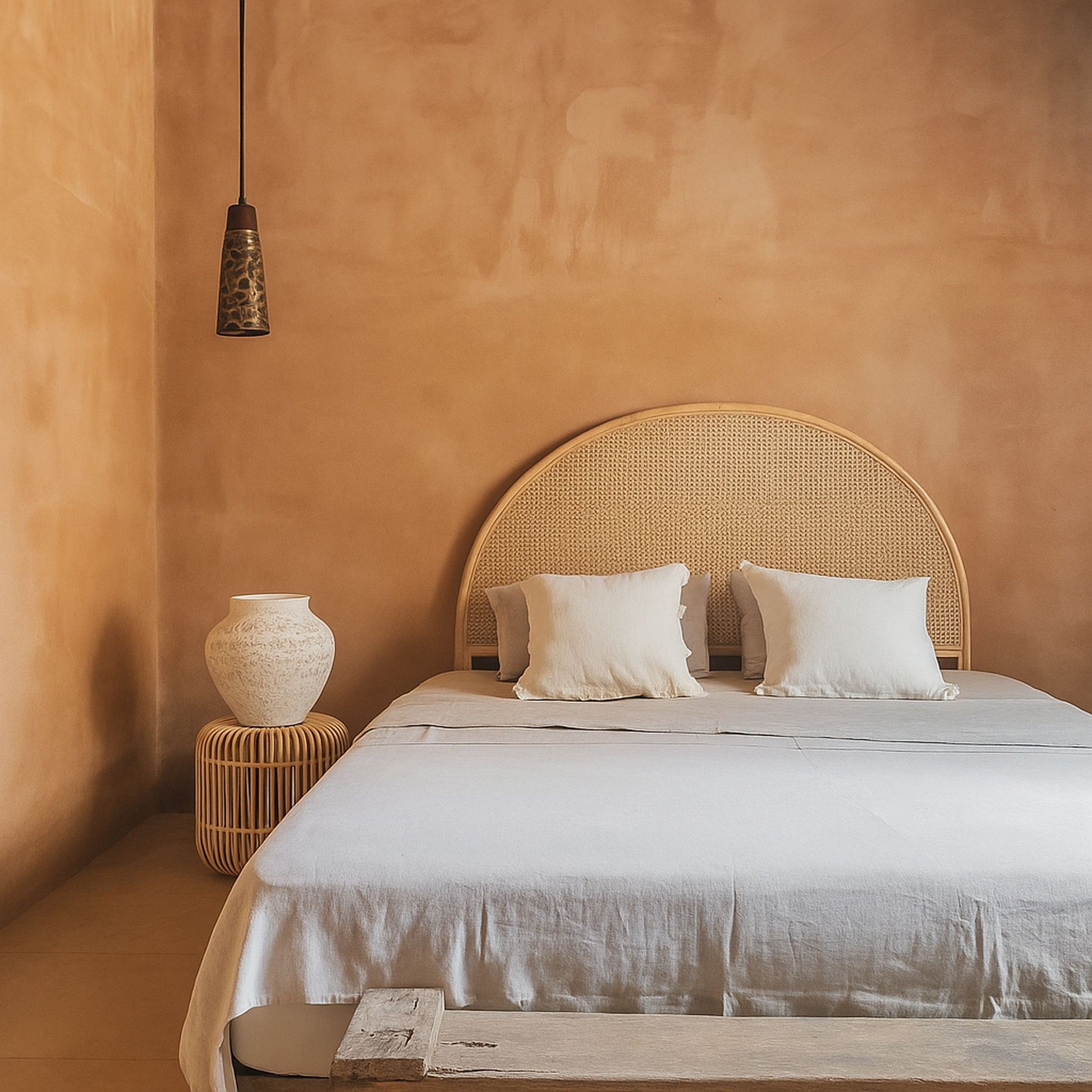 Bedroom with a wicker headboard and white bedding against a warm-toned wall.