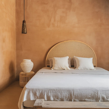 Bedroom with a wicker headboard and white bedding against a warm-toned wall.