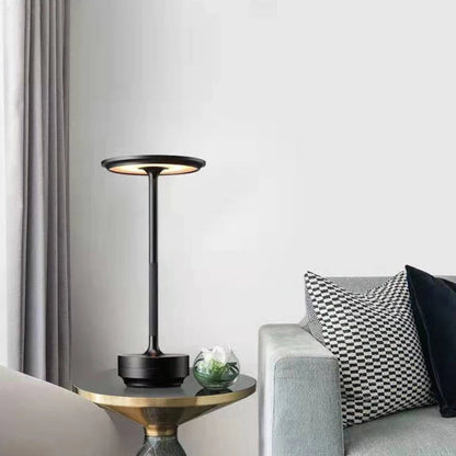 Modern black table lamp on a side table with a gray sofa and decorative pillows in a living room setting.