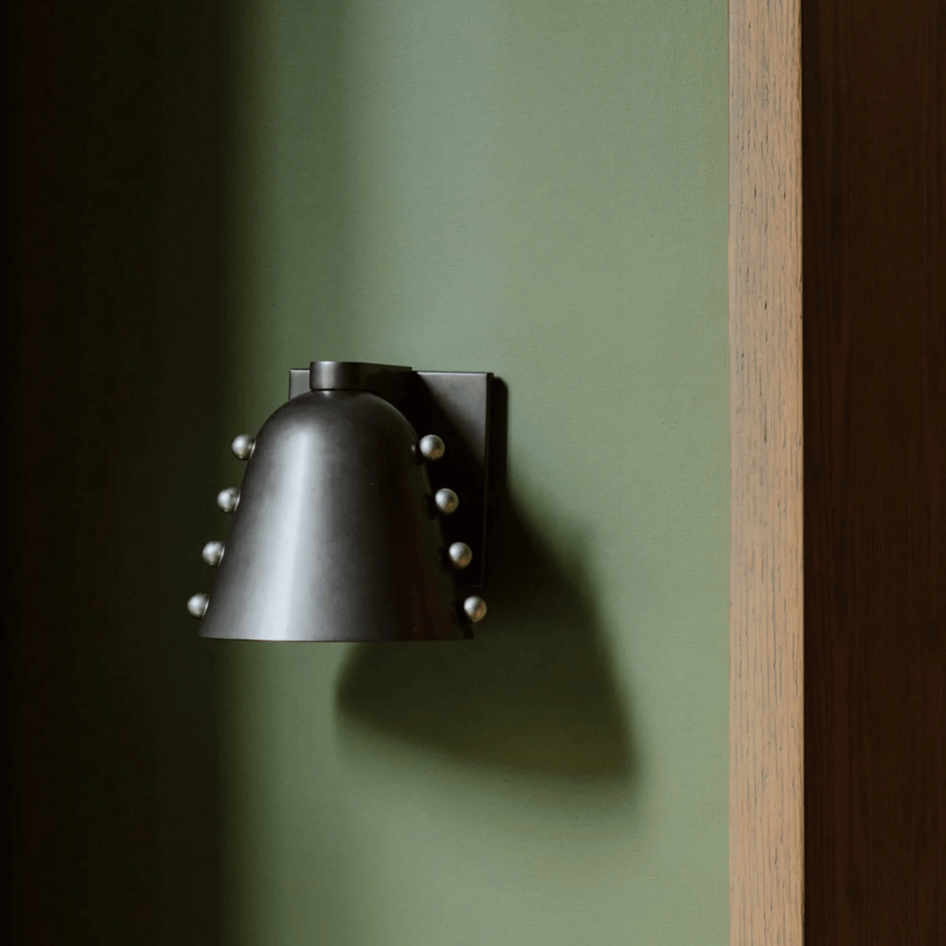 Black wall-mounted light fixture on a green wall with a wooden frame.