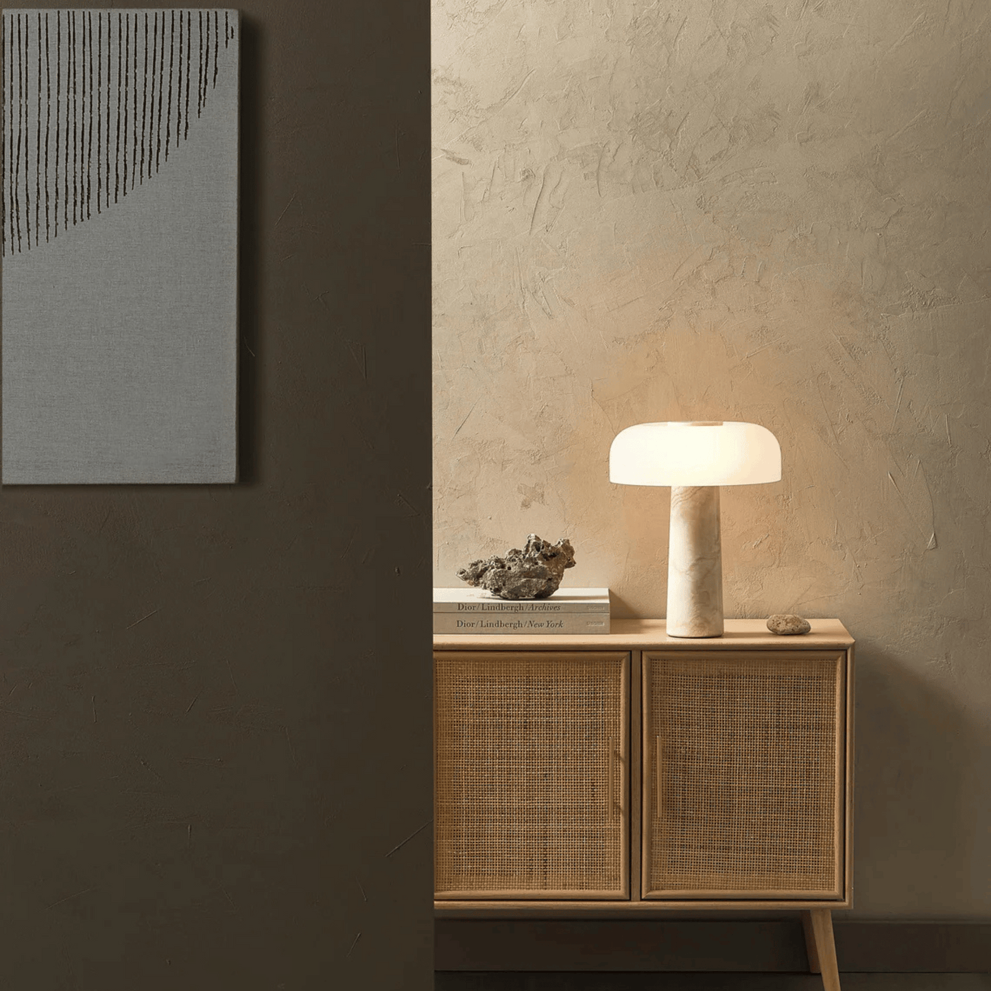Nest table lamp on a wooden cabinet against a textured wall with abstract art.