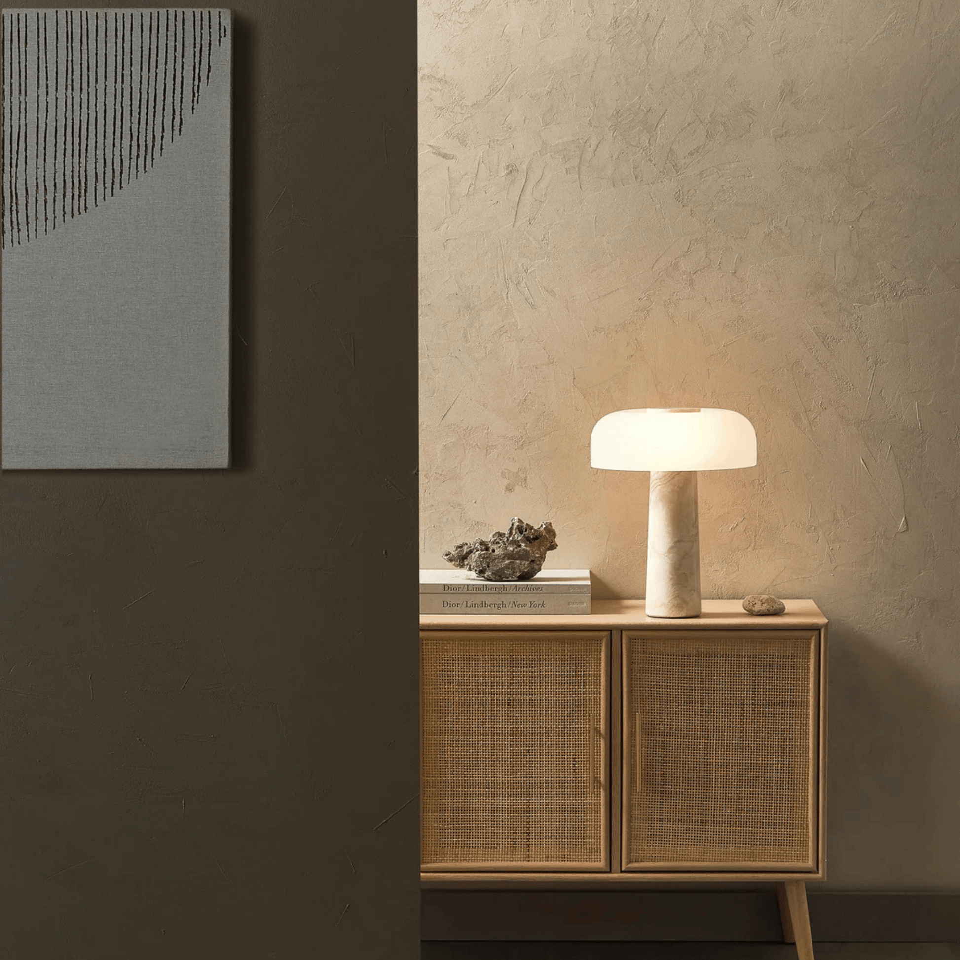 Nest table lamp on a wooden cabinet against a textured wall with abstract art.